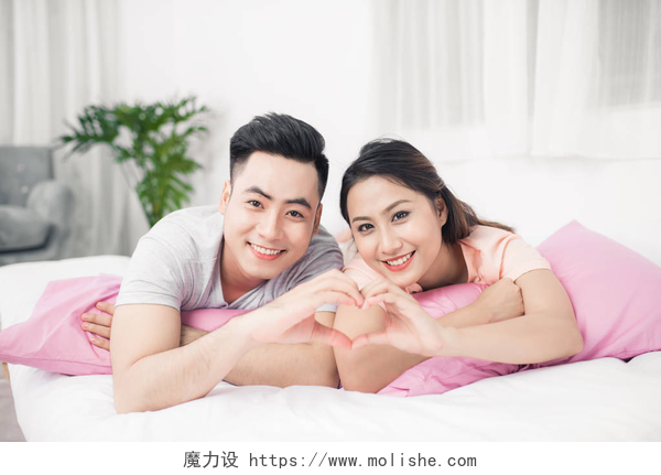 躺在床上比心的年轻浪漫夫妇肖像躺在床上的夫妻